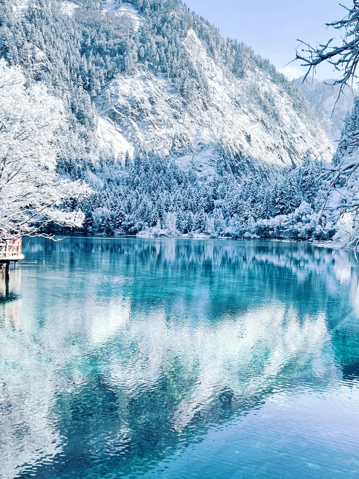 Turquoise alpine lake reflecting snow-covered mountains and winter forests in China